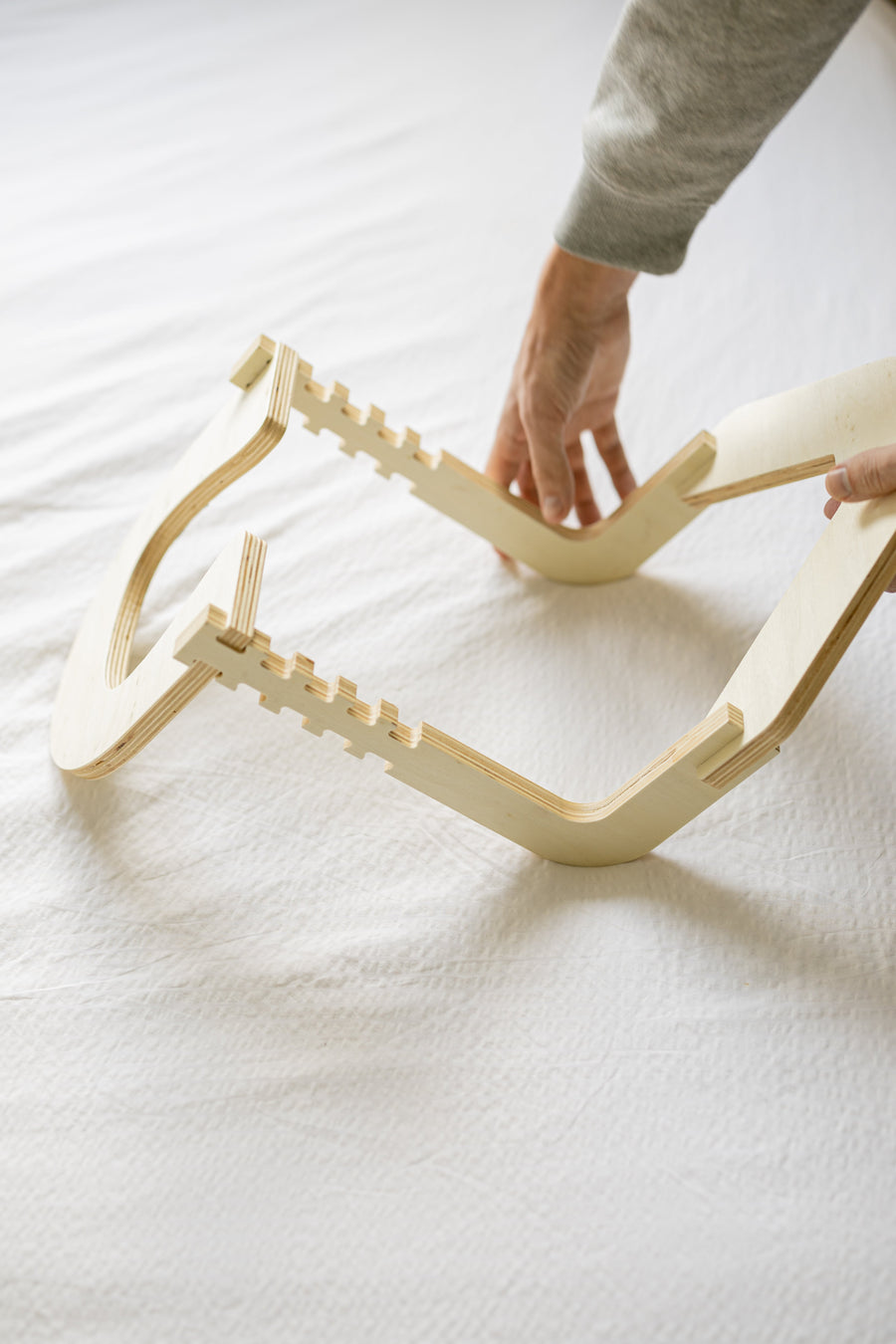 Hands assemble the wooden frame on a made bed