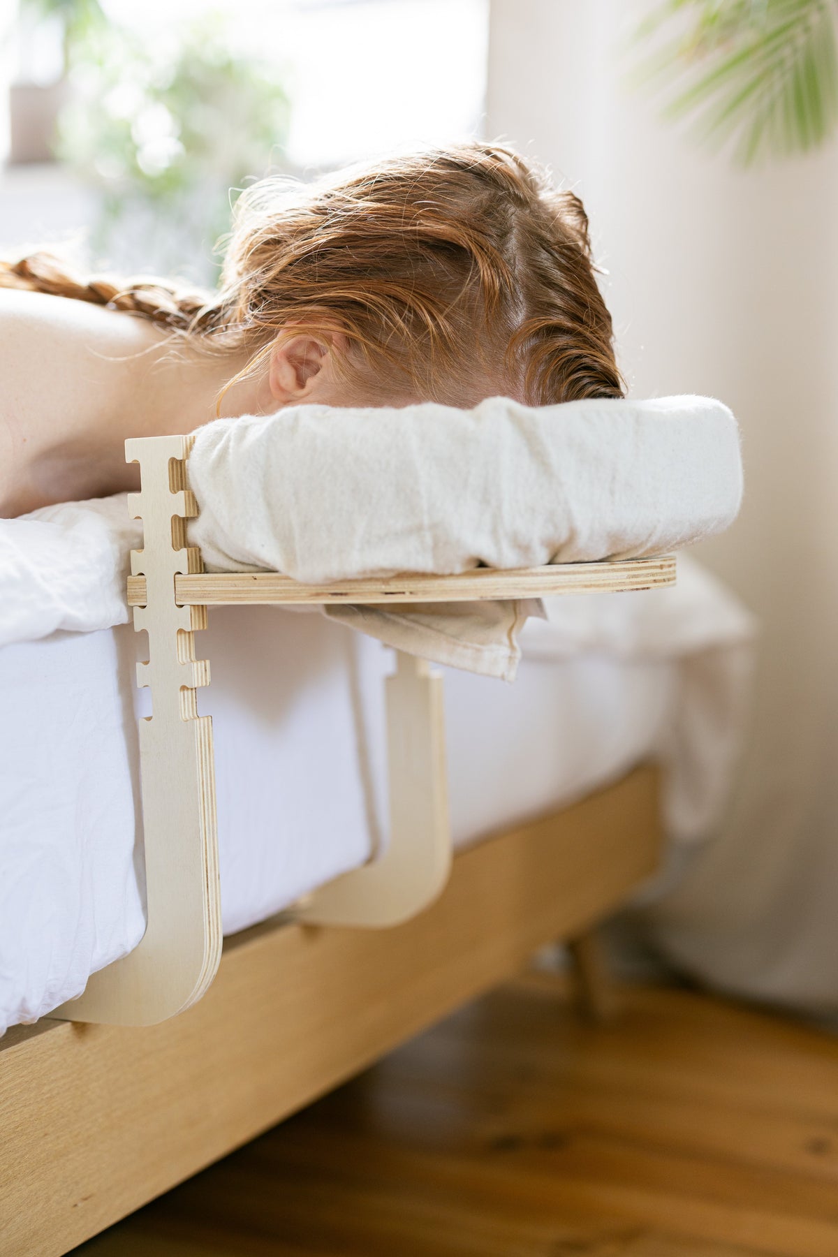 Woman with a braid lying with her head in the headrest at the edge of the bed